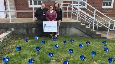 Woman standing in front of court house with blue CAC pinwheels in grass lawn